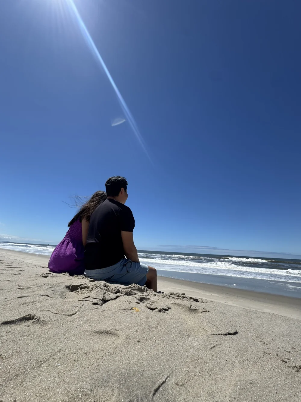 Tiago e Angelys sentados na areia, olhando o mar